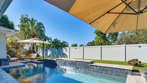 Una piscina con bordes de azulejos, rodeada de un patio con sillas y sombrillas.