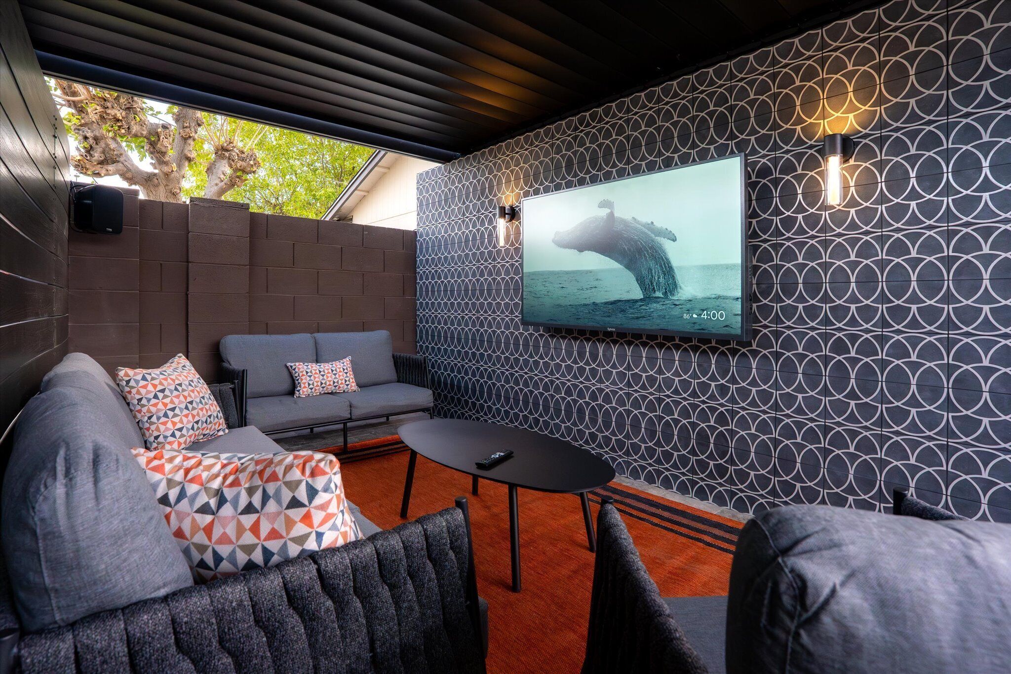 Un espace de détente extérieur moderne, aménagé avec un canapé, des fauteuils et une table. Un grand écran diffuse une image de baleine.