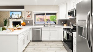 Una cocina moderna con armarios blancos, electrodomésticos de acero inoxidable, lavavajillas y un amplio ventanal con vistas al exterior.