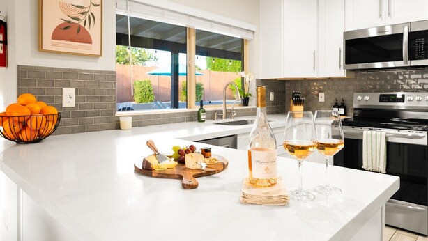 Una cocina moderna con armarios blancos, un ventanal grande y una encimera con una botella de vino y copas.