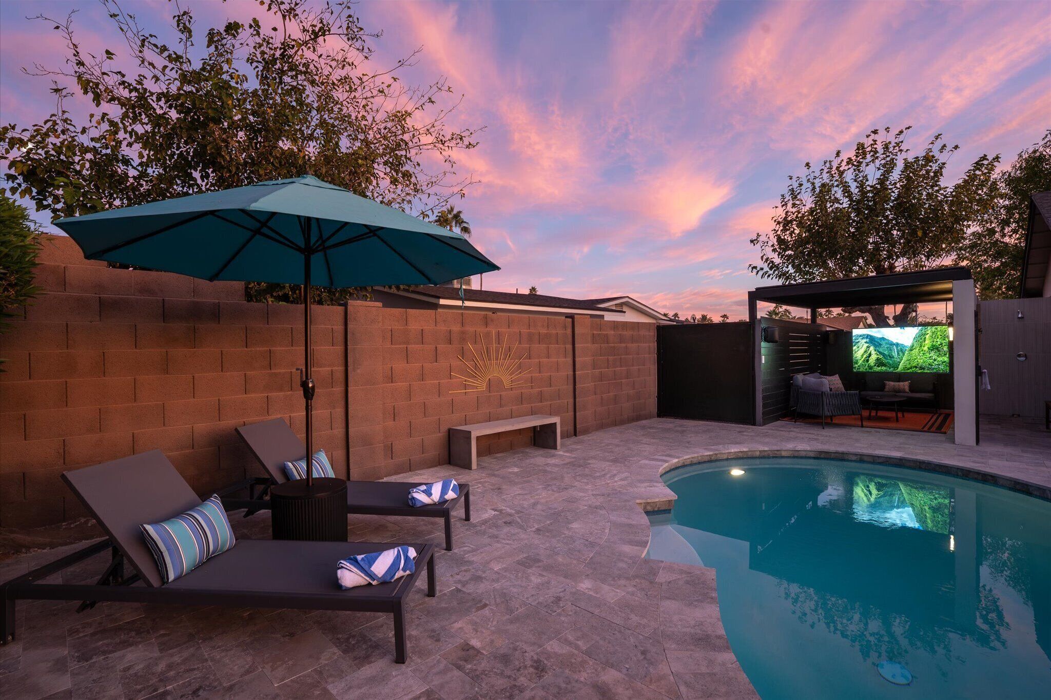 A backyard with a swimming pool, lounge chairs, a bench, and a covered seating area.
