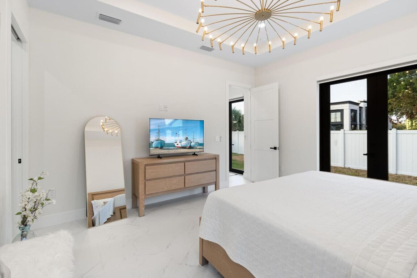 Quarto moderno com uma cama grande, uma TV sobre uma cômoda de madeira, e vista para o exterior por uma porta deslizante.
