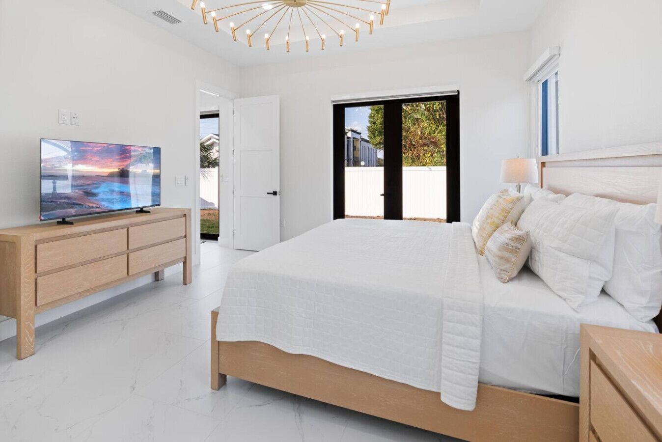 A bedroom with a bed, a TV on a wooden dresser, and a view of the outside.