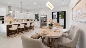 Una cocina moderna con armarios blancos, una isla central con taburetes y luminarias colgantes.