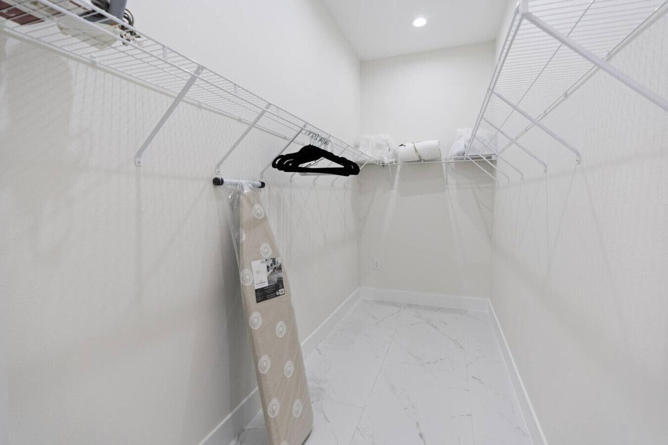 A small, white-walled room with a shower area, a towel rack, and a small shelf with toiletries.