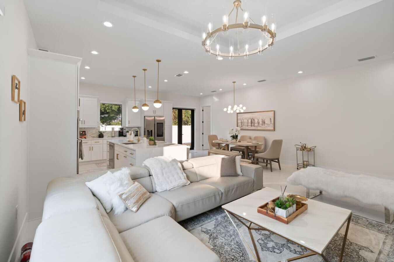 A modern living room with a sectional sofa, a coffee table, and a dining area with a chandelier.