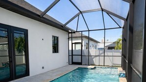 Una piscina con cerramiento de vidrio, agua azul cristalina y solárium con baldosas.