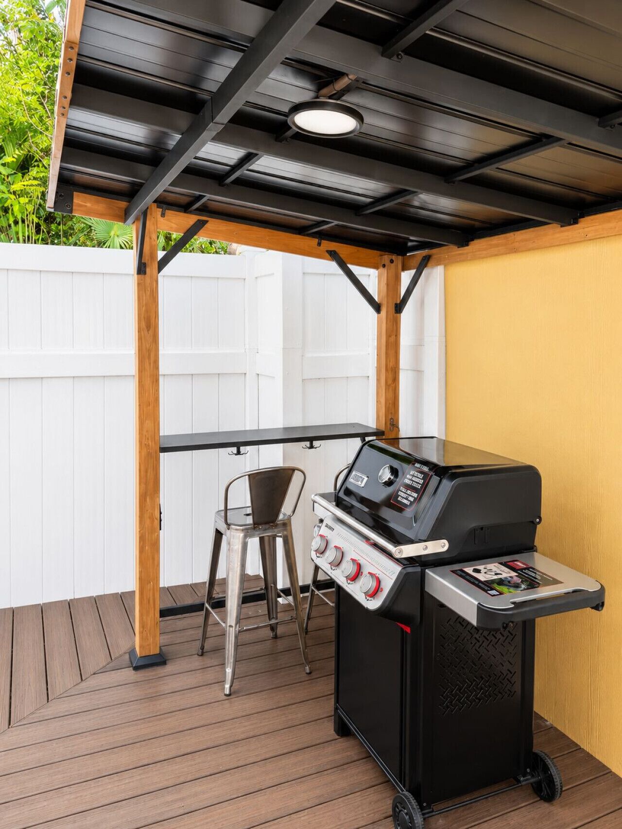 Un patio al aire libre con una parrilla, una silla de metal y una mesa de madera.
