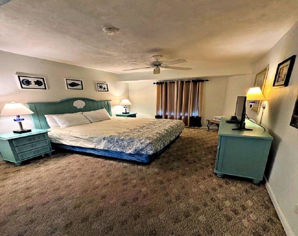 Ein Schlafzimmer mit einem Bett, zwei Nachttischen mit Lampen, einem Deckenventilator und einem Fenster mit Vorhängen.