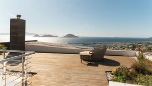 Una terraza de madera con una silla y vista al mar e islas distantes.