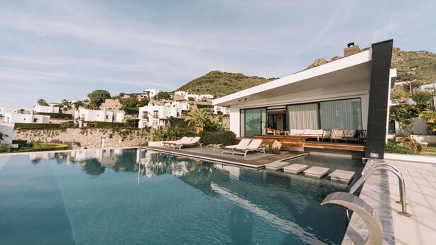 Un área de piscina moderna con sillas de descanso y un edificio con grandes ventanales.