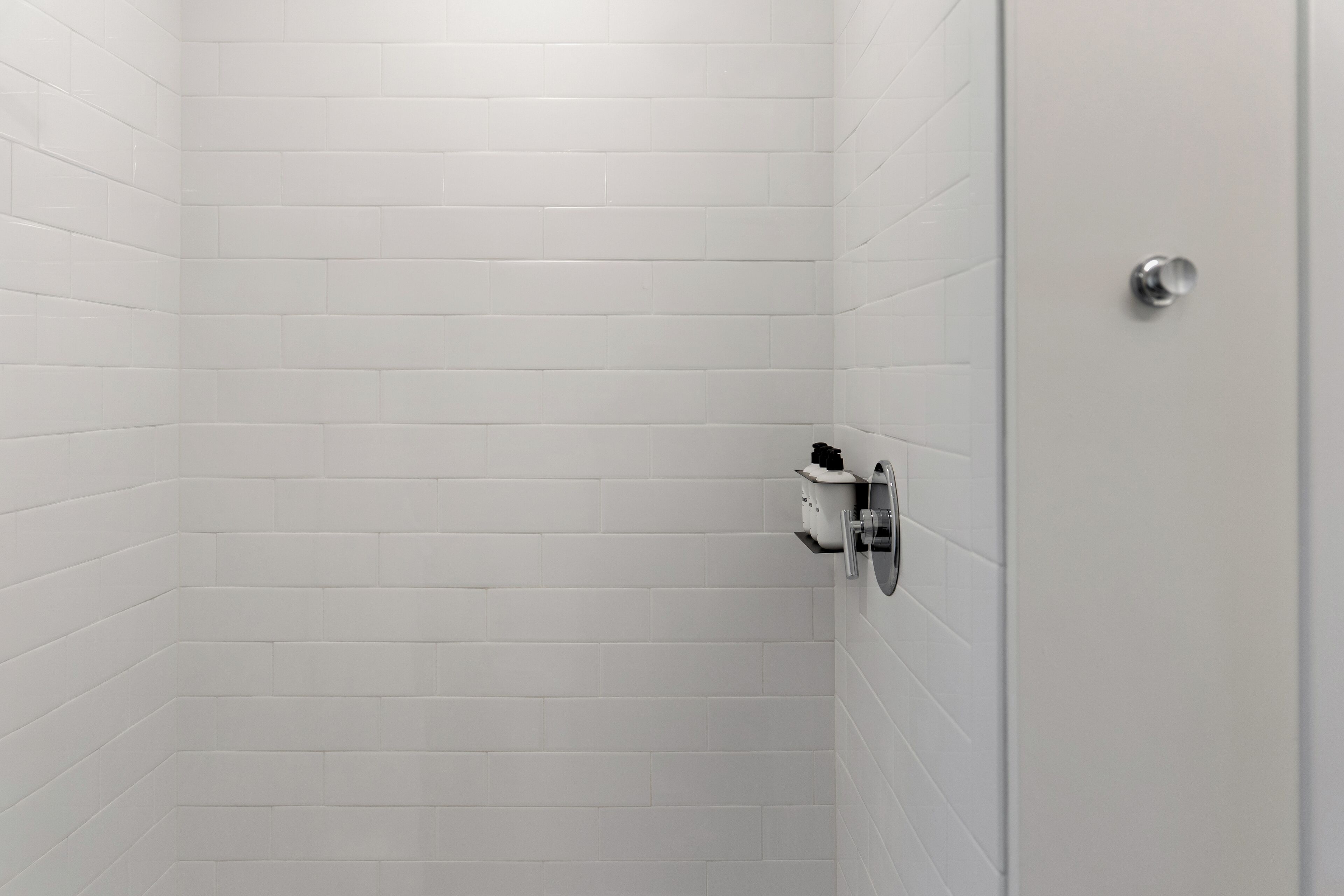 A bathroom with white tiled walls and a door with a silver handle.