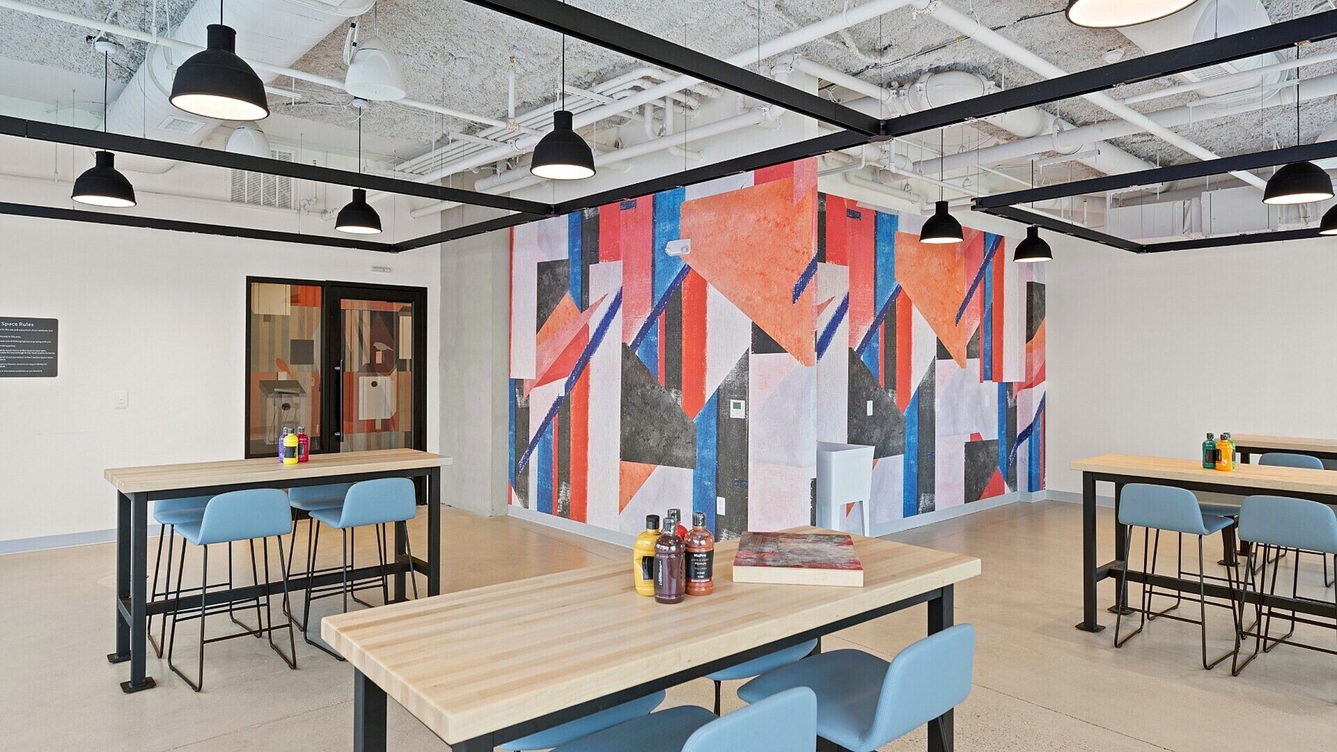 A modern office space with high ceilings, exposed ductwork, and a vibrant abstract mural on the wall.