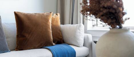 A sofa with two pillows, a blue throw blanket, and a vase with dried plants.
