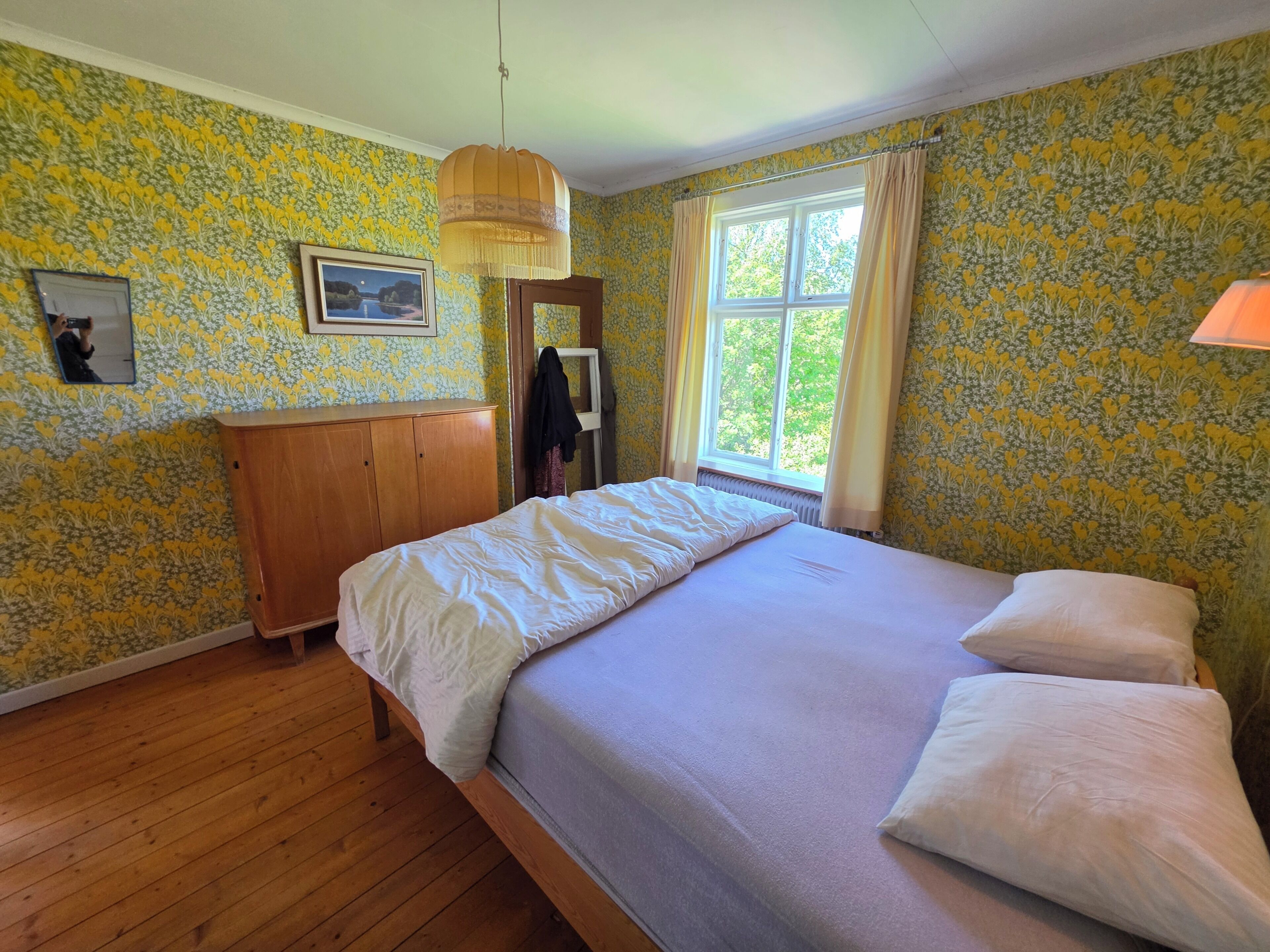 A bedroom with a wooden bed, a mirror, a picture on the wall, and a window with curtains.