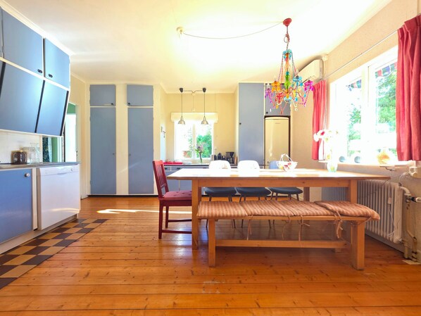 Een keuken met blauwe kastjes, een eettafel met stoelen, een hanglamp en uitzicht op groen.