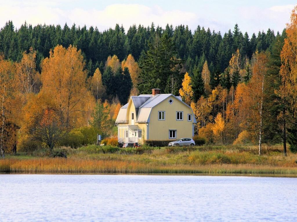 Ett hus med ett sluttande tak, en skorsten och ett garage, omgivet av en skog med träd i höstfärger.