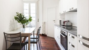 A modern kitchen with white cabinets, a built-in oven, and a dining area with a wooden table and chairs. - Easylife - Milan - italia 11 P4 - Historic Center (Milano)