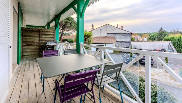 A covered outdoor area with a table and chairs, a wooden fence, and a view of the surrounding neighborhood. - Charming apartment with pool, near center and lake, sleeps 4 (Sanguinet)