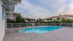 A swimming pool with a metal ladder, surrounded by a white fence and a paved deck. - Charming apartment with pool, near center and lake, sleeps 4 (Sanguinet)