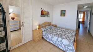 Een slaapkamer met een bed, een nachtkastje, een lamp, een kledingkast en een schilderij aan de muur.