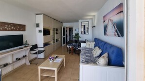Een woonkamer met een televisie, bank en een eethoek met een tafel en stoelen.
