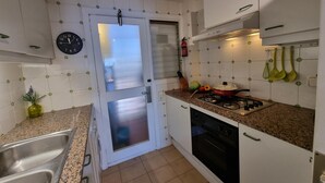 Een kleine keuken met witte kastjes, een roestvrijstalen spoelbak, een fornuis en een klok aan de muur.