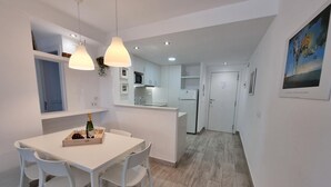 Una cocina moderna con armarios blancos, un comedor con mesa y sillas blancas, y una pequeña isla con una botella y vasos.