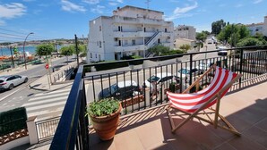 Ein Balkon mit Blick auf eine Küstenstraße, einem Blumentopf und einem gestreiften Liegestuhl.