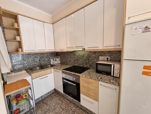 Uma cozinha compacta com armários brancos, micro-ondas, fogão e geladeira.