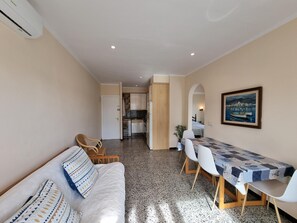 Um espaço compacto com cozinha compacta, área de jantar com mesa e cadeiras, sofá com almofadas estampadas e um quadro na parede.