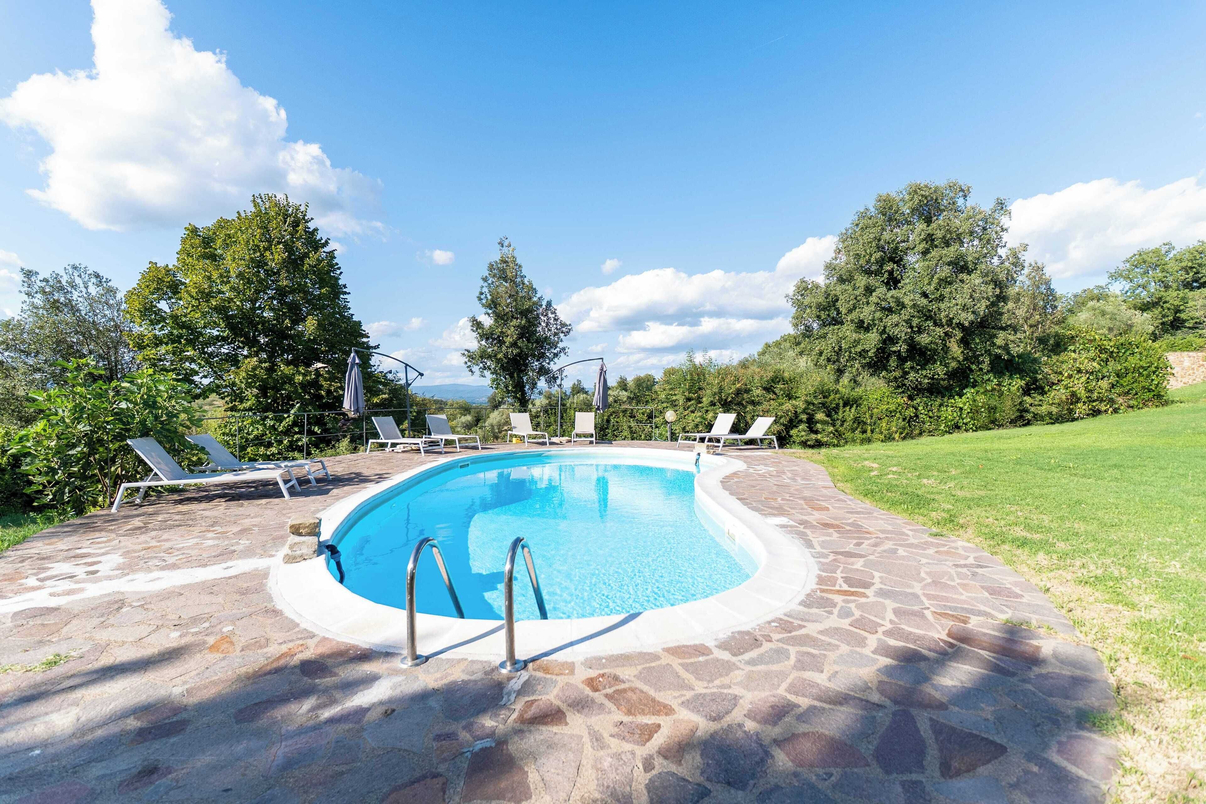 Une piscine aux bords recouverts de pierres, entourée de chaises longues et de verdure.
