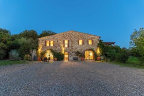 A stone building with a gravel driveway, large windows, and outdoor seating. - La Fornace - Luxury Tuscan Retreat with Spa (Toscana)