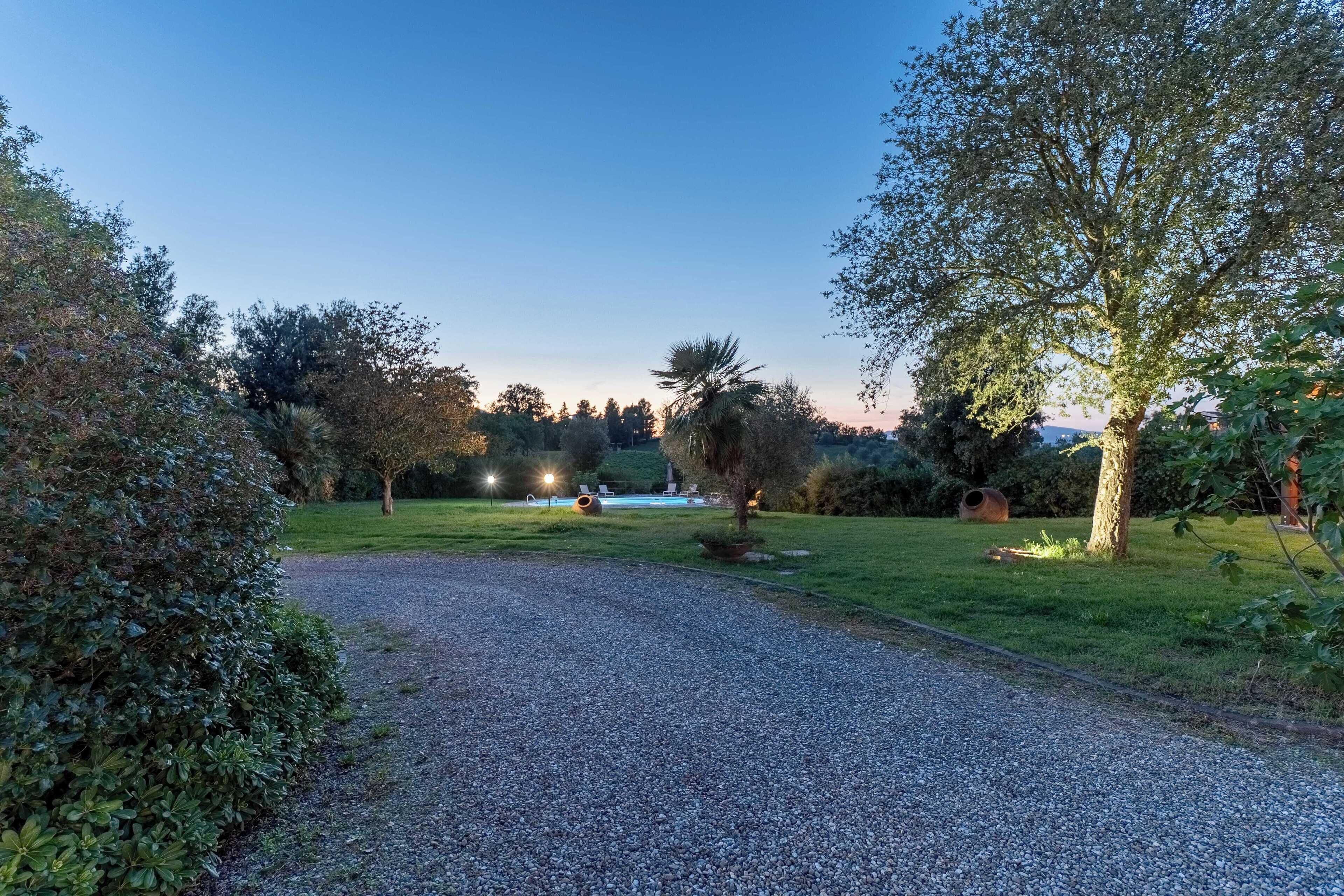 A gravel path leading to a pool area with surrounding greenery and trees.