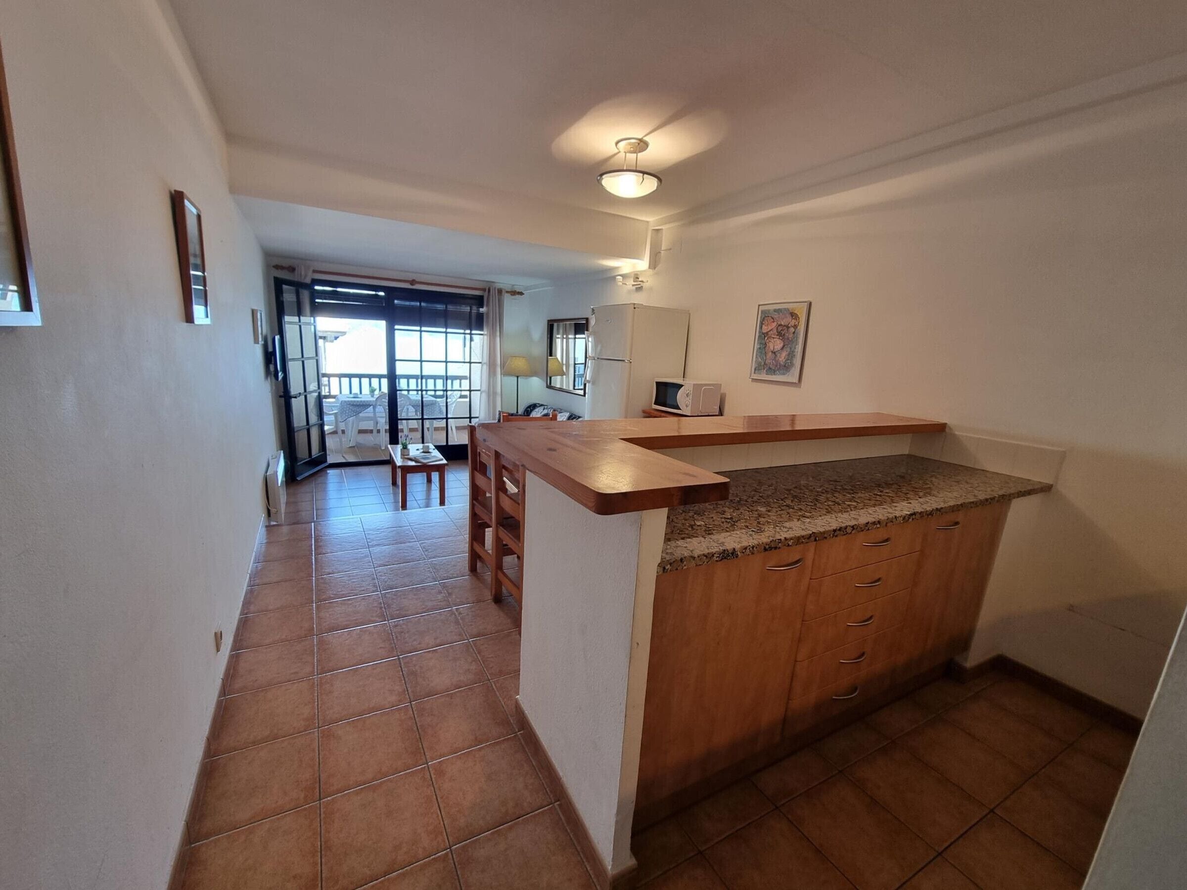 A kitchen with a wooden counter and cabinets, a dining area with a table and chairs, and a view of the outside through a glass door.
