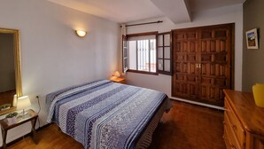 A bedroom with a bed, a dresser, a nightstand, a mirror, a window with bars, and a door. - Cozy apartment with terrace 400m from the beach (L'Escala)