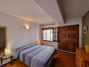 A bedroom with a bed, a dresser, a nightstand, a mirror, a window with bars, and a door. - Cozy apartment with terrace 400m from the beach (L'Escala)