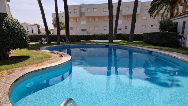 A swimming pool with clear blue water, surrounded by a well-maintained lawn and palm trees. - Cozy apartment with terrace 400m from the beach (L'Escala)