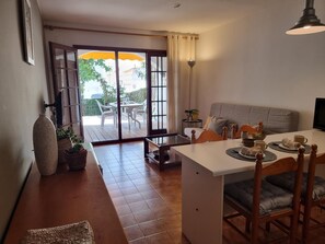 A cozy living area with a sofa, dining table, and chairs. There is a sliding glass door leading to an outdoor patio with a table and chairs. - Cozy apartment with terrace 400m from the beach (L'Escala)