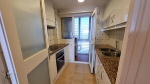 Eine kompakte Küche mit weißen Schränken, einem Backofen, einer Spüle und einem Fenster mit Jalousien.