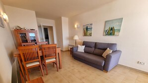 Ein Wohnzimmer mit grauem Sofa, einem Holzespeisetisch, Stühlen, einem Fernseher und zwei Bildern an der Wand.