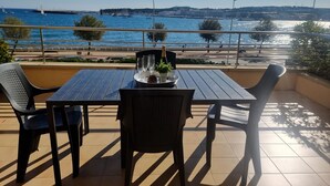 Eine Terrasse mit Tisch für zwei Personen, mit Blick auf ein Gewässer mit Booten und eine ferne Stadtansicht.