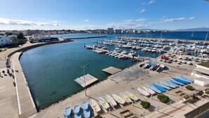 Een jachthaven met afgemeerde boten, een gebogen oever en een stadszicht op de achtergrond.