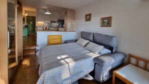 Ein gemütliches Schlafzimmer mit einem Bett, einem Nachttisch, einer Couch und einem kleinen Tisch. Im Hintergrund ist eine Küche zu sehen.