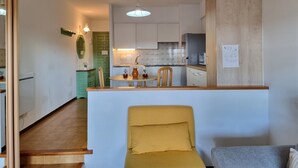Ein kompakter Wohnraum mit Küche, Essbereich und einer kleinen Sitzecke mit gelbem Sessel und grauem Sofa.
