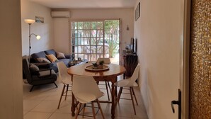 Ein Wohnzimmer mit einer Couch, einem Esstisch mit Stühlen, einer Stehlampe und einem Fenster mit Blick auf Bäume.