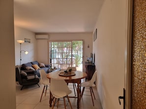 Ein Wohnzimmer mit einer Couch, einem Esstisch mit Stühlen, einer Stehlampe und einem Fenster mit Blick auf Bäume.