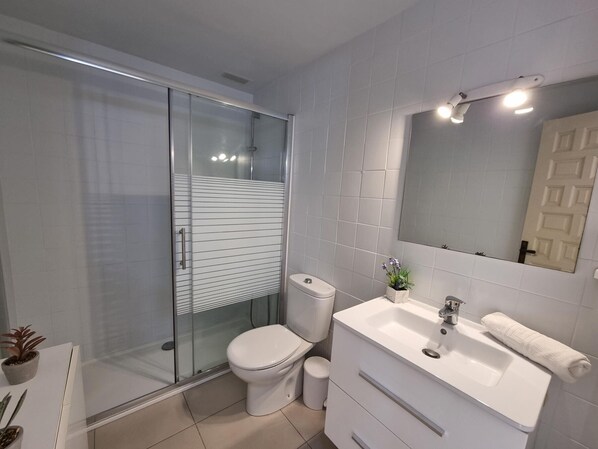 Une salle de bain moderne avec une douche à parois de verre, des toilettes, un lavabo avec un miroir et une plante en pot.