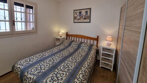 Ein Schlafzimmer mit Bett, Nachttisch, Lampe, einem Fenster mit Gitterstäben und einem Bild an der Wand.