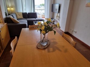 A dining table with a vase of yellow flowers, a sofa, a television, and a view of the outdoors. - Cozy apartment near the beach with air conditioning (L'Escala)